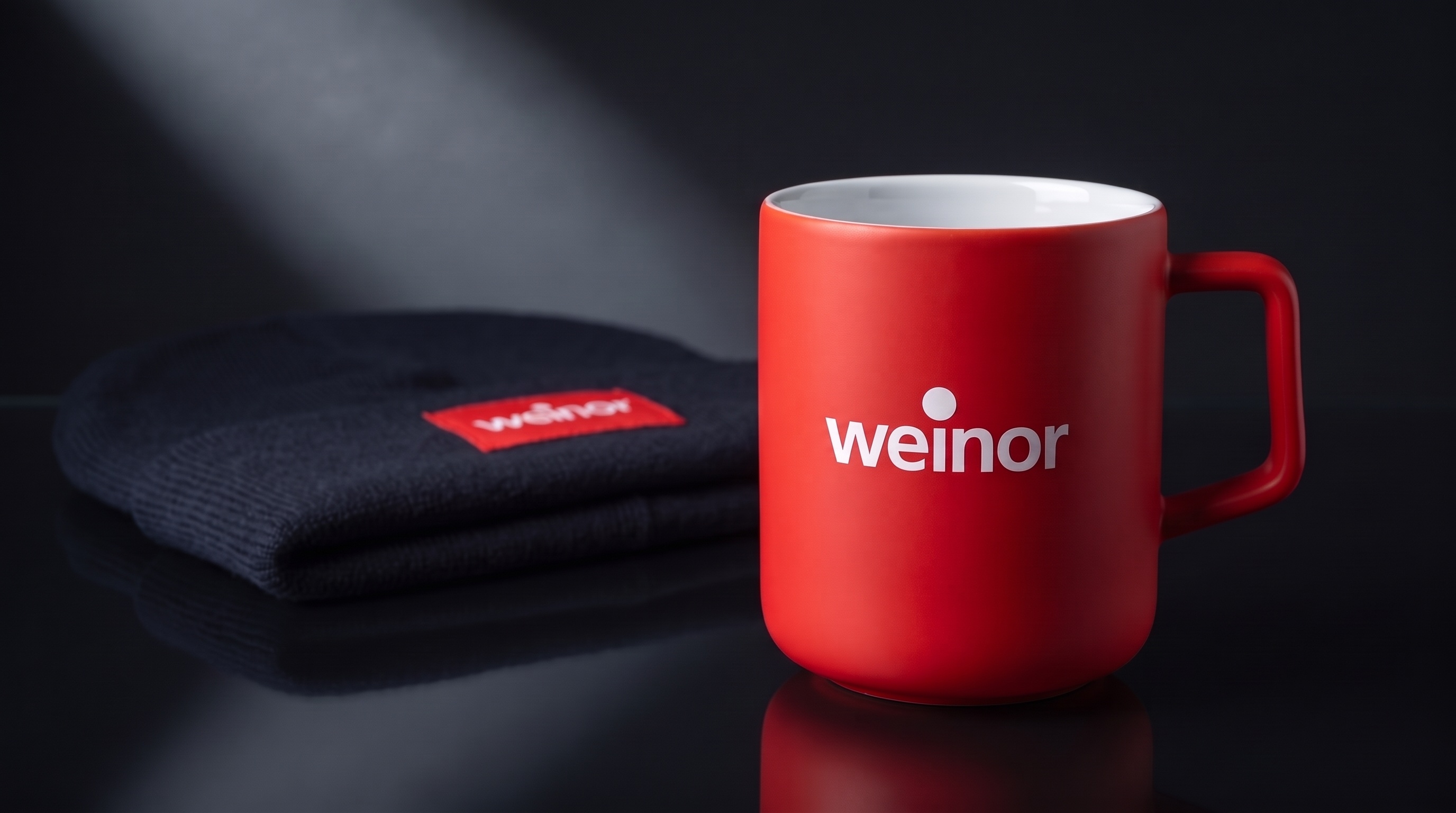 Rote weinor Tasse und dunkler Beanie mit weinor Label im Lichtstrahl